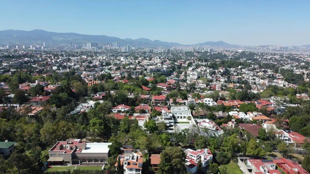 Vista aérea de una zona residencial de casas entre árboles, con la ciudad al fondo