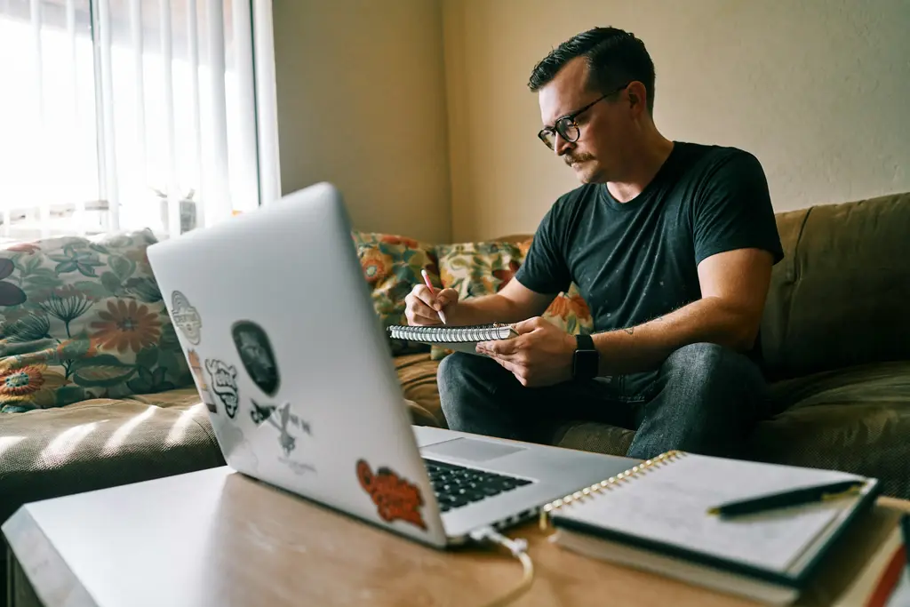 Profesional estudia en casa con una computadora portátil y toma notas