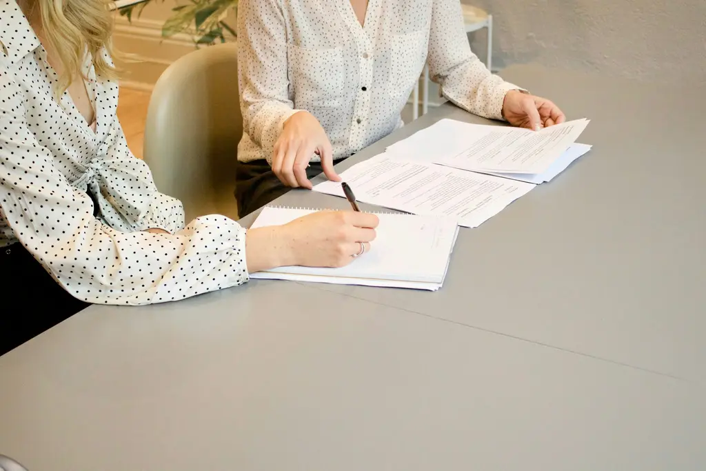Dos personas firman documentos sobre un escritorio