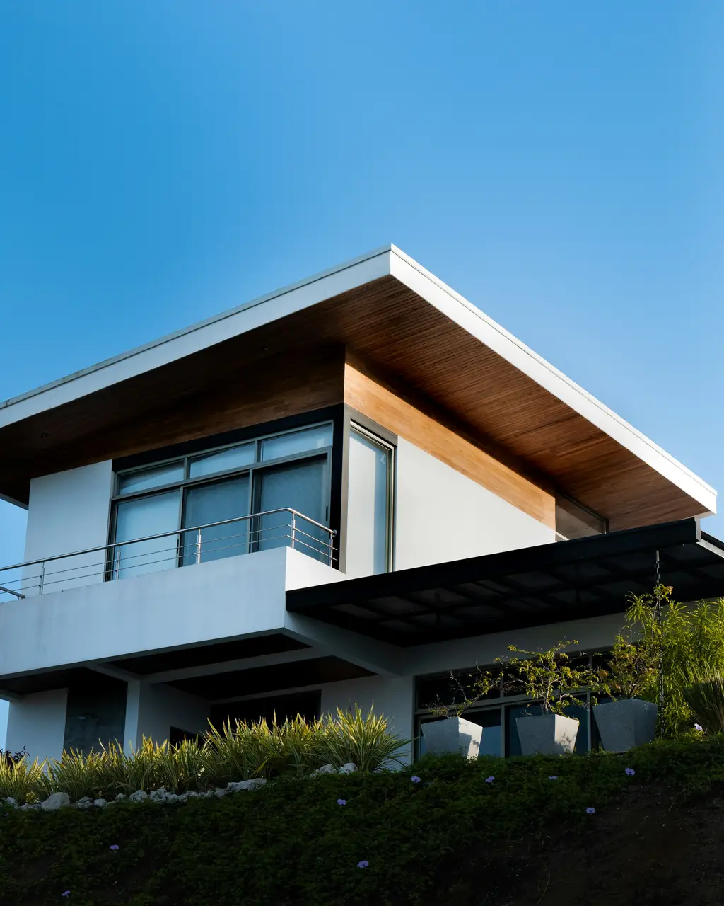 Casa contemporánea de dos plantas con alero de madera y jardín, bajo cielo despejado